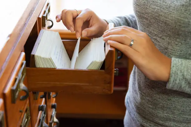 Photo of Librarian opens the library card index. Young woman open catalog file box. Database concept and Education Concept