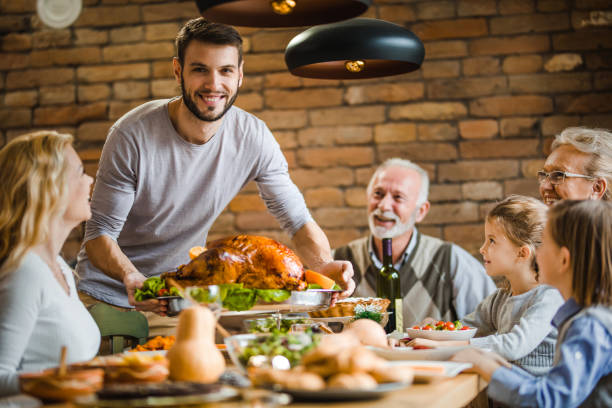 молодой счастливый человек, обслуживающий свою семью, набитую индейкой на ужин в честь дня благодарения за обеденным столом. - thanksgiving turkey dinner dinner party стоковые фото и изображения