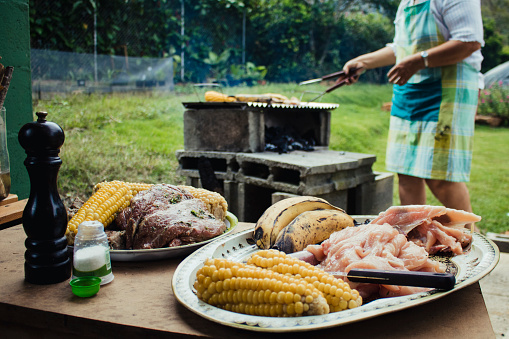 A woman out in the garden cooking on a BBQ featuring traditional Colombian food including Plantains and Maize.