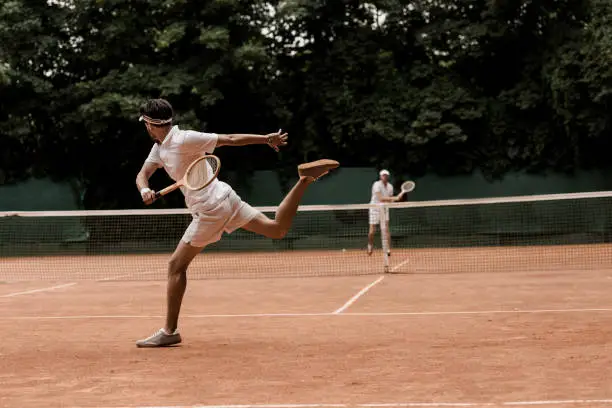 Photo of retro styled men playing tennis at court