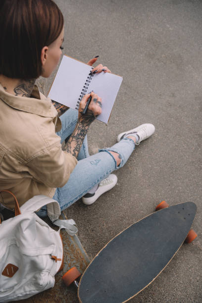 istock high angle view of tattooed woman with skateboard writing in empty textbook 1002079756