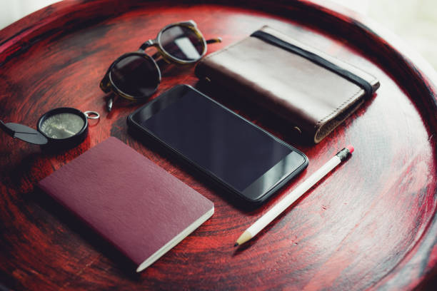 istock Set of mobile, passport ,notebook,sunglasses,compass and white pencil on rustic red wood round table near window.Tropical Summer Holiday vacation concept.clipping path on smartphone screen. 1002087228