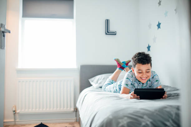 ragazzo che usa il tablet digitale al mattino - bed child smiling people foto e immagini stock