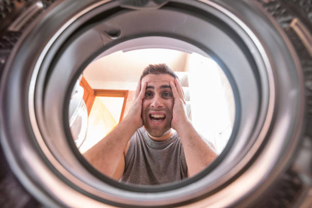 istock Shocked upset Young man Looking At Stained Bleached Cloth In Washing Machine. View from the inside of washing machine. 1002097740