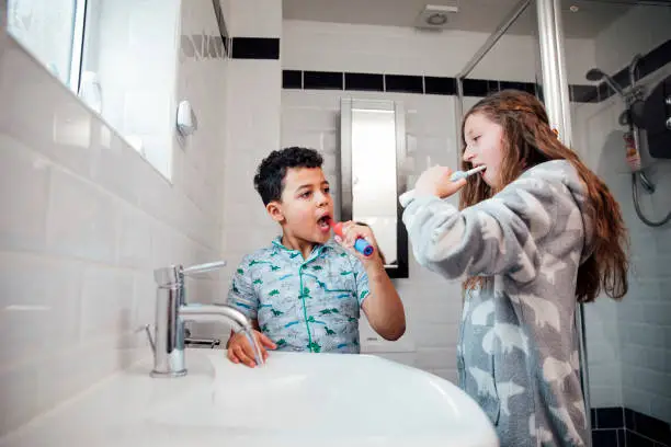 Little boy and his older sister are brushing their teeth together in the bathroom at home.