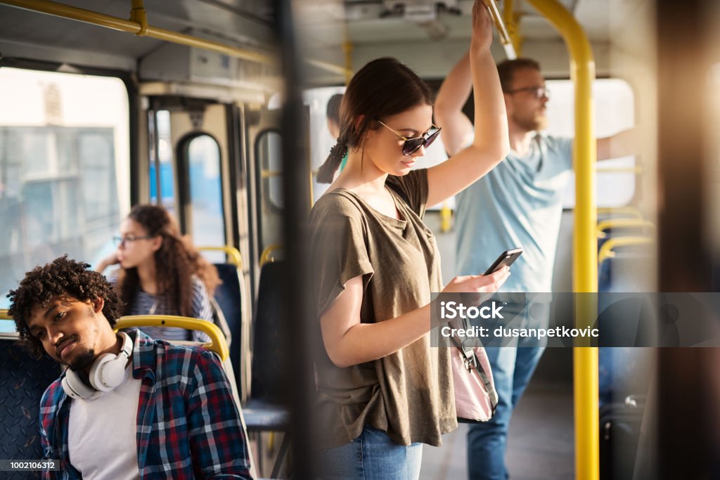 Sweet girl with sunglasses in using phone while standing in a bus. Bus Stock Photo