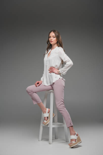 istock elegant female model sitting on chair and looking at camera on grey background 1002109234