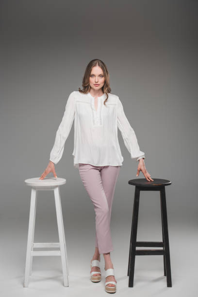 istock elegant woman posing between two chairs on grey background 1002109308