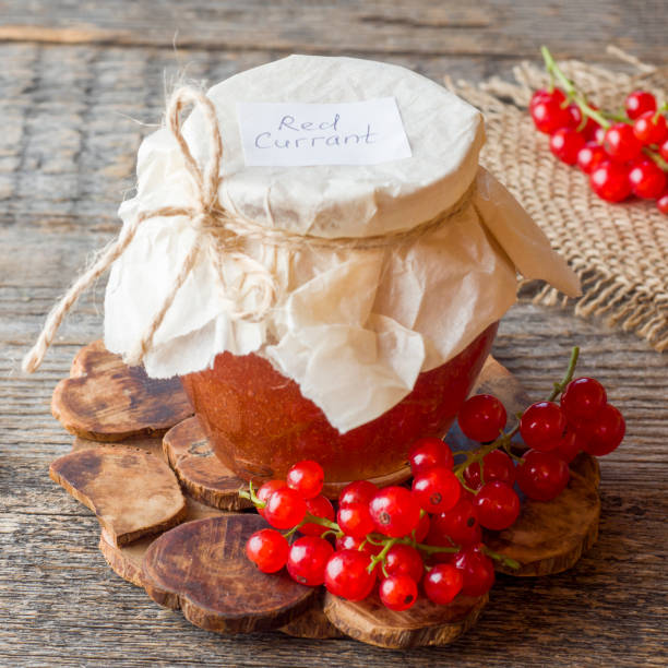 istock Useful currant jam in a glass jar. Fresh red currant on wooden background 1002112362