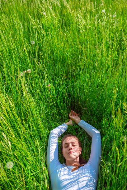 Beautiful woman man with hands on chest, closed eyes and grateful face gesture lying in the klee grassland. Useful for healthy, mindfulness, consciousness, awareness and self love concepts. Very selective focus and added grain. Part of a series.