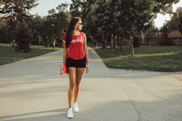 Woman with a skateboard walking through the park on a sunny day