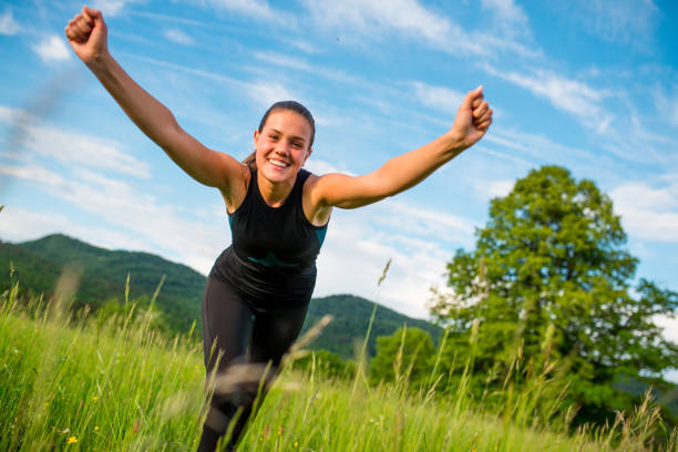Young Cheerful Woman with Arms Outstretched Standing on Meadow.