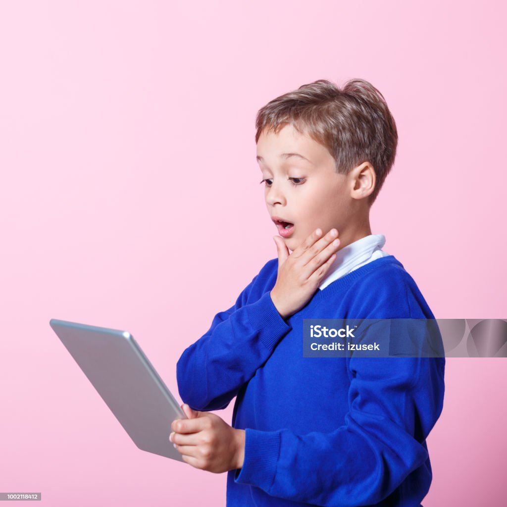 Portrait of surprised schoolboy using a digital tablet Surprised schoolboy wearing school uniforms using a digital tablet. Studio shot, pink background. Education Stock Photo