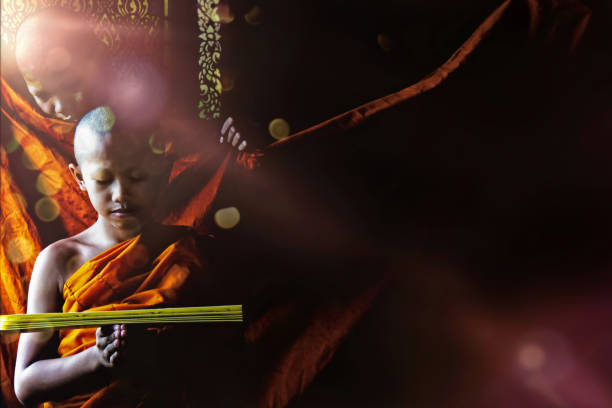 istock A young Thai Buddhist novice reading Buddhism scripture and another novice standing and look at behind with sun flare through window 1002118536