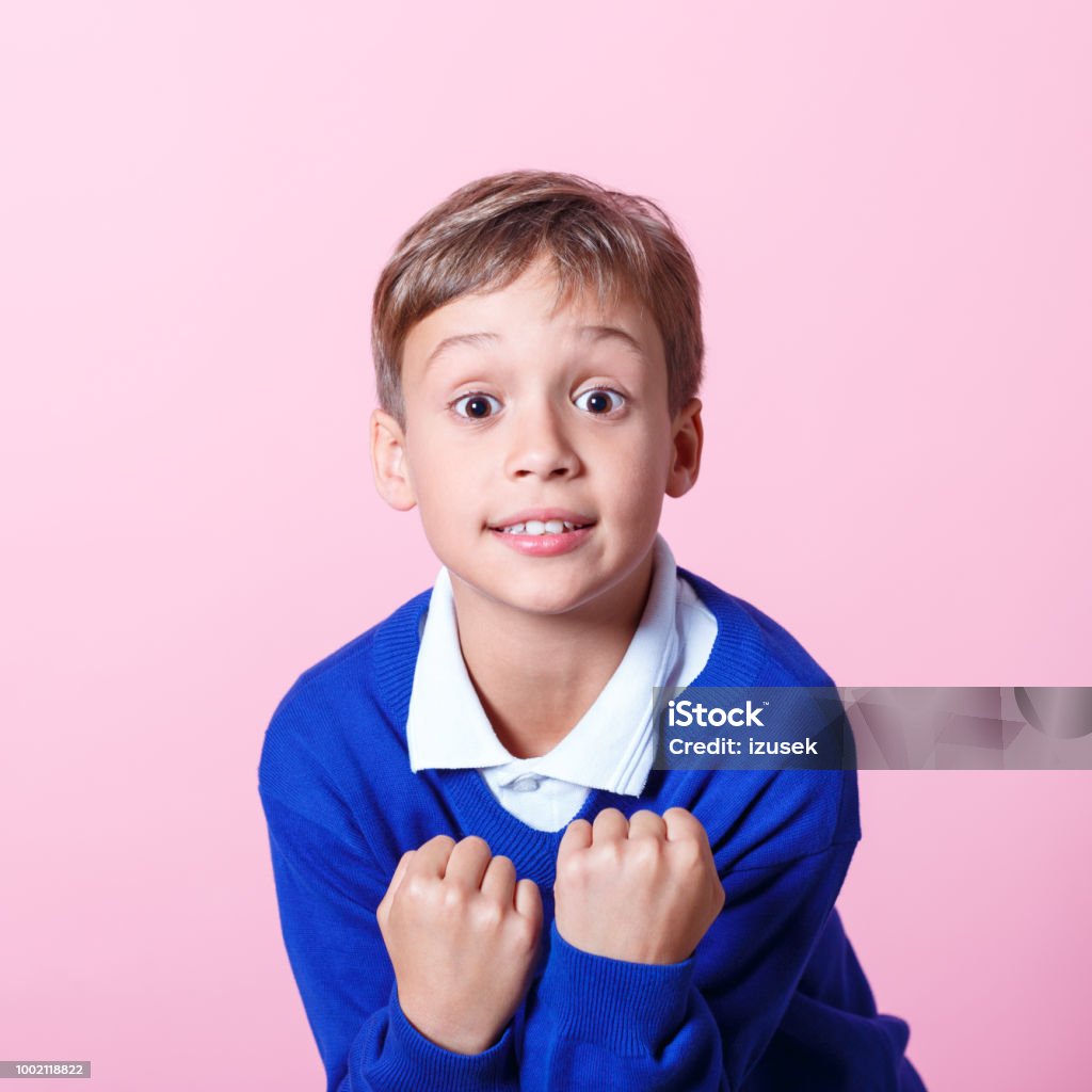 Portrait of excited schoolboy cheering against pink background Excited schoolboy wearing school uniforms clenching his fists. Studio shot, pink background. Child Stock Photo