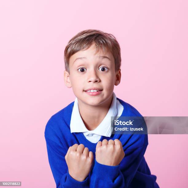 Portrait Of Excited Schoolboy Cheering Against Pink Background Stock Photo - Download Image Now
