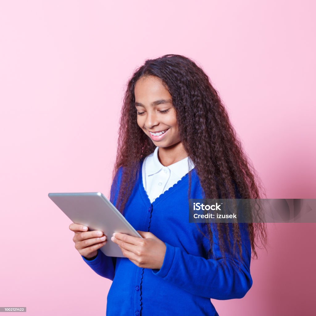 Portrait of happy afro amercian schoolgirl using digital tablet Afro American schoolgirl wearing school uniforms using a digital tablet. Studio shot, pink background. Digital Tablet Stock Photo