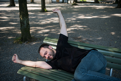 Young man lying down sleep on bench in the park and wakes up after rest.