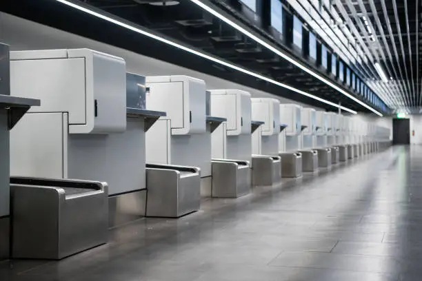 Photo of Interior of check-in area in modern airport: luggage accept terminals with baggage handling belt conveyor systems, multiple information LCD screen, indexed check-in desks