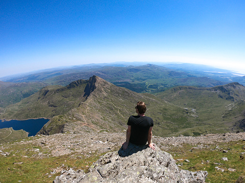 A hiker looks out  from the summit of Mount Snowdon, Wales, UK. Mount Snowdon stands at 1,085 Meters above sea level.