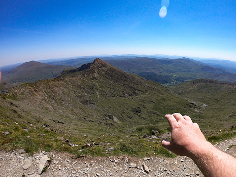 A mans hand reaches out over the views from the summit of Mount Snowdon, Wales, UK. Mount Snowdon stands at 1,085 Meters above sea level.