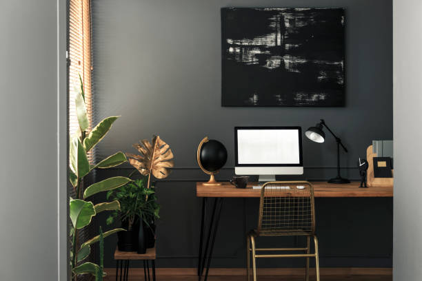 istock Painting above desk with computer desktop and lamp in grey and gold workspace interior. Real photo 1002133058