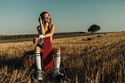 Beautiful teenage girl with a skateboard sitting in the grass on a summer day