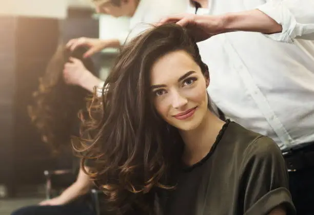 Happy woman sitting at beauty salon, making beautiful evening hairstyle with curls, copy space