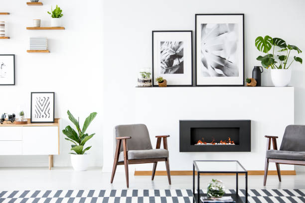 istock Fireplace between grey armchairs in modern living room interior with posters and plants. Real photo 1002148280