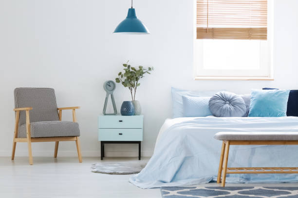 istock Plant on cabinet between patterned armchair and blue bed in bedroom interior with lamp. Real photo 1002149264