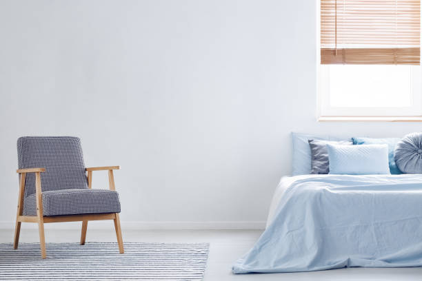 istock Patterned armchair on carpet in minimal bedroom interior with blue bed and copy space. Real photo 1002149294
