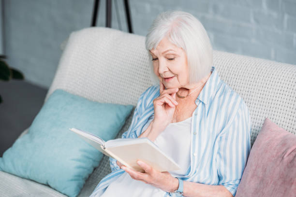 istock senior woman reading book while resting on sofa at home 1002153350