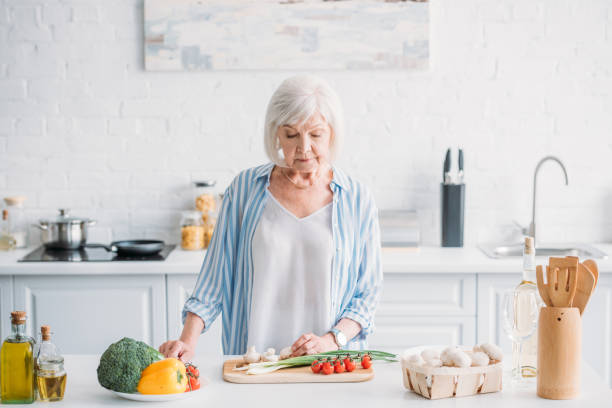 istock portrait of senior lady cutting vegetables while cooking dinner at counter in kitchen 1002153414