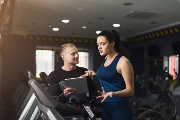 istock Fitness coach helps woman on elliptical trainer 1002154698