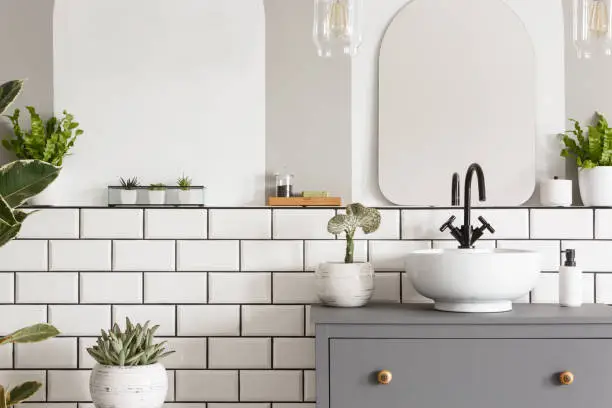 Photo of Real photo of a sink on a cupbaord in a bathroom interior with tiles, mirror and plants