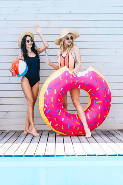 istock beautiful young girlfriends holding bottles with summer drinks and beach items at poolside 1002175554