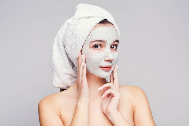 Beautiful girl with applied clay mask at white background