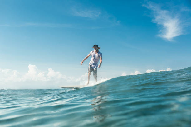 distant view of male surfer riding in ocean at nusa dua beach, bali, indonesia - bali male beautiful ethnicity imagens e fotografias de stock