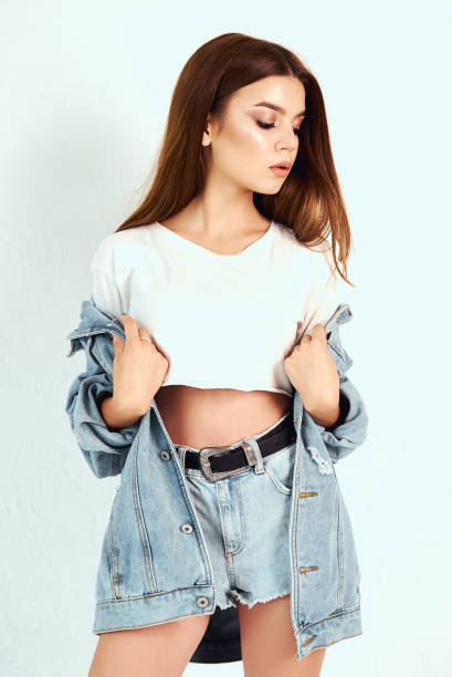 istock A girl in a denim jacket and short shorts. Posing in the studio on a white background 1002194084