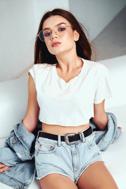 A girl in a denim jacket and short shorts. Posing in the studio on a white background
