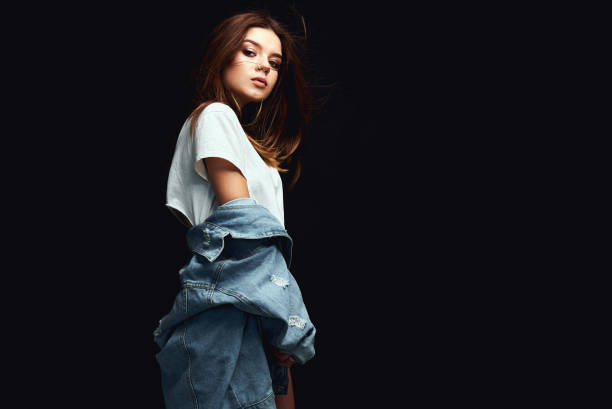 istock A girl in a denim jacket and short shorts. Posing in the studio on a white background 1002194362