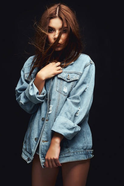 istock A girl in a denim jacket and short shorts. Posing in the studio on a white background 1002194540