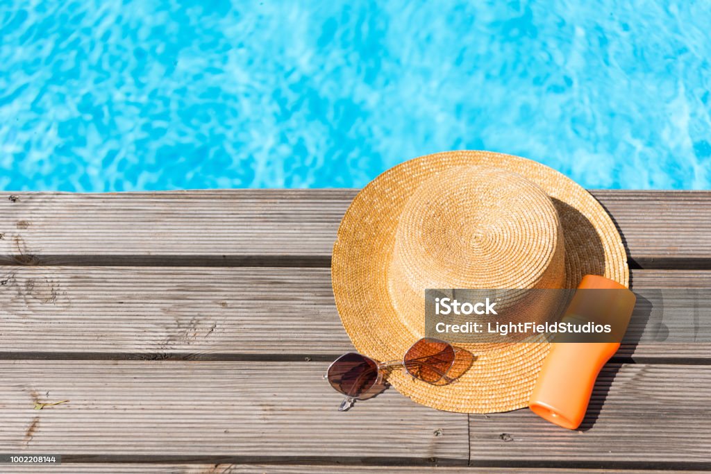 top view of wicker hat, sunglasses and sunscreen near swimming pool Poolside Stock Photo