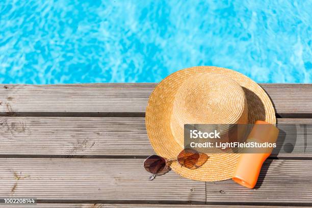 Top View Of Wicker Hat Sunglasses And Sunscreen Near Swimming Pool Stock Photo - Download Image Now