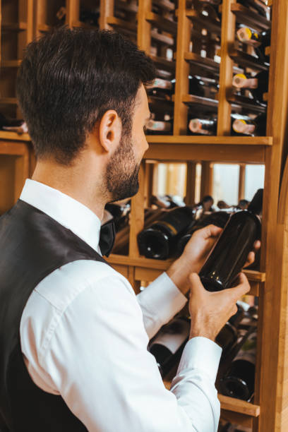 istock handsome young sommelier taking bottle from shelf at wine store 1002216148