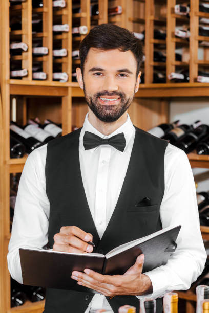istock handsome young wine steward making notes and looking at camera at wine store 1002216292
