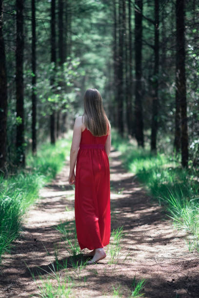 istock Blonde woman in red dress on forest path. 1002222822