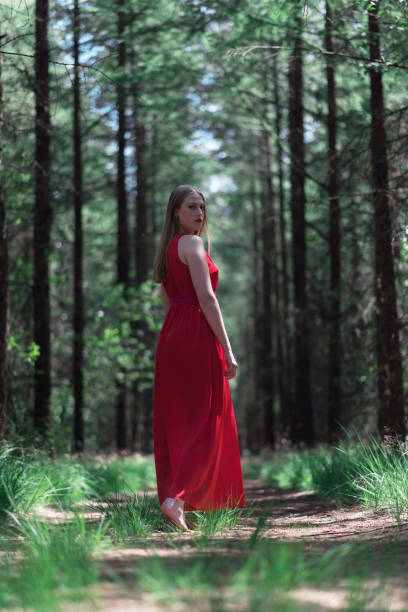 istock Blonde woman in red dress on forest path looking over shoulder. 1002222934
