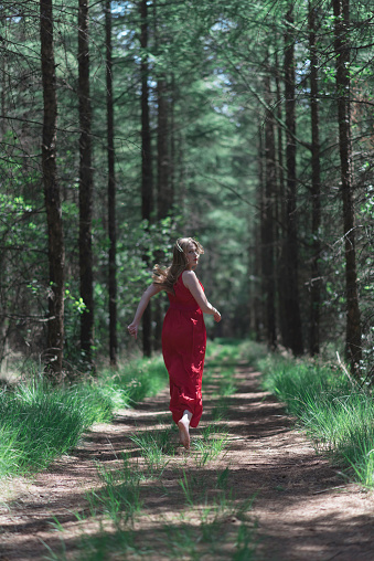 Blonde woman in red dress running away from camera on forest path.