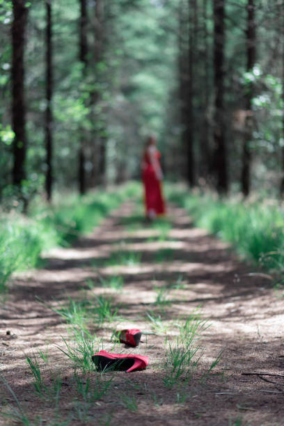 Red shoes fallen on forest path with blurred woman in background.